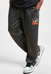 Grå sweatpants med et tæt waistband, der har et orange og hvidt "GUARDS" logo. Bæres med hvide og grå sneakers.