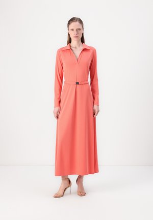 Long coral dress with a collar, v-neckline, and a cinched waist featuring a belt. Smooth fabric with long sleeves. Worn with tan high heels.