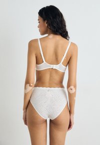 Reggiseno bianco in pizzo con spalline regolabili e chiusura a gancio, abbinato a slip bianchi a vita alta con un bordo smerlato.