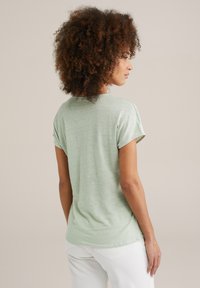 T-shirt vert clair à manches courtes avec une coupe décontractée, fabriqué en tissu doux et texturé, avec un col rond et un discret détail de couture au dos.