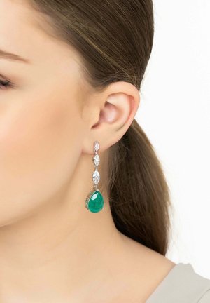 Dangle earrings with a green teardrop gemstone, silver accent stones, and intricate detailing, hanging below the earlobe.