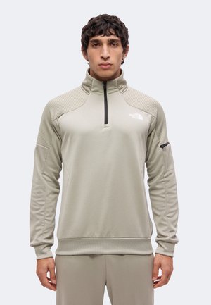 Homme portant un pull à demi-fermeture éclair gris clair avec des panneaux texturés aux épaules et une poche zippée sur la manche gauche.