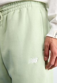 Svetlozelené jogger nohavice z mäkkej bavlnenej zmesi, s elastickým pásom a bielym vyšívaným logom na stehne. Hladký povrch, voľný strih.