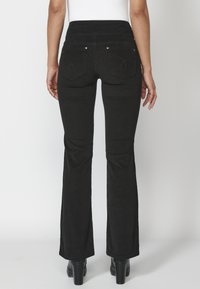Jeans negros de campana con una cintura alta, que cuentan con dos bolsillos traseros y detalles de costura sutiles. El material es denim con una textura suave.