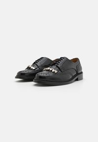 Scarpe di pelle nera con dettagli decorativi a punta d'ala, accenti di cucitura a contrasto e abbellimenti metallici lucidi sulla tomaia.
