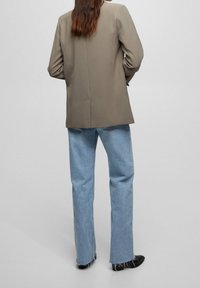 Beige struktureret blazer med et enkelt spil, båret over lyseblå denimbukser med frynset kant og sorte sko.