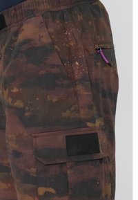 Cargo-byxor i ett flerfärgat mönster av brunt och orange. Har en sidficka med lila dragsko och en svart logotypmärkning.