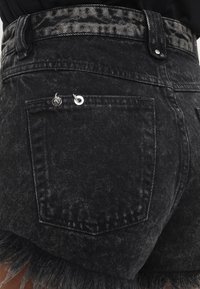 Mustat farkkushortsit korkealla vyötäröllä, joissa on reikäytynyt helma, pieni takatasku ja metalliset yksityiskohdat. Teksturoitu kangas, jossa on haalistunut kuvio.