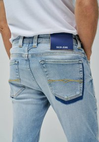 Vaqueros de denim azul claro con costuras amarillas, con una etiqueta navy en la cintura, acabados con dos bolsillos traseros y detalles deshilachados.