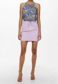 Bloemrijke haltertop met blauwe en paarse patronen; roze mini-jurk met verstelbare taille. Stiletto-hakken maken de outfit compleet.
