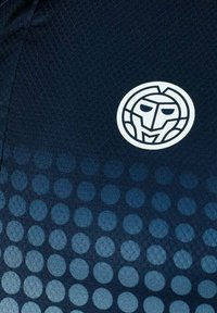 Marineblaue Kurzarmbluse mit einem kreisförmigen Logo, das ein stilisiertes Gesicht zeigt. Gepunktetes Muster, das von dunklen zu hellen Farbtönen übergeht.