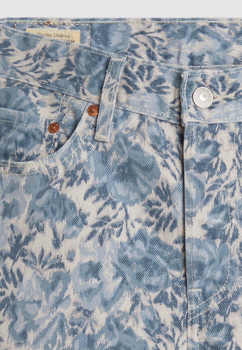 Tissu en denim à motif floral dans des nuances de bleu variées, avec des boutons en cuivre, une poche avant et un design de taille standard.