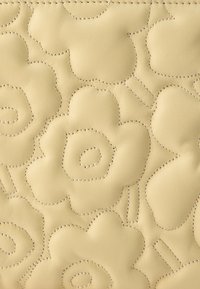 Krémová koža s vyrazeným kvetinovým vzorom, so zreteľným šitím. Hladká textúra s vystupujúcimi tvarmi kvetov a jemnými detailmi.