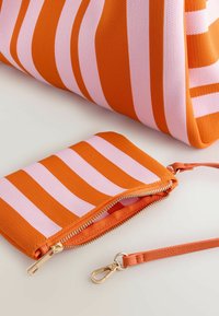 Trousse en tissu rayé orange et rose avec une fermeture éclair dorée et une sangle orange avec un fermoir en métal, posée sur une surface claire.