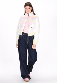 Irideszcens, rövidített pufi dzseki magas gallérral, két elülső zsebbel és világosbarna bordázott mandzsettával. Széles lábú sötét farmernadrággal és rózsaszín cipőkkel párosítva.