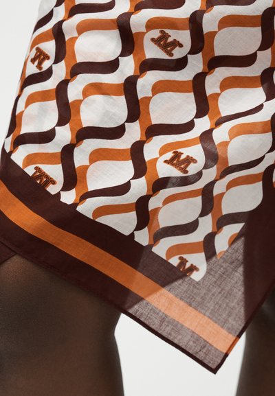 Καφέ, πορτοκαλί και λευκή φούστα με κυματιστές ρίγες και μοτίβα με το γράμμα "M", φορεμένη πάνω από πόδι με σκουρόχρωμο δέρμα.