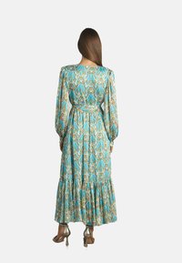 Robe longue turquoise à motifs avec des manches bouffantes, taille cintrée et jupe à volants. Présente des motifs floraux et géométriques complexes.