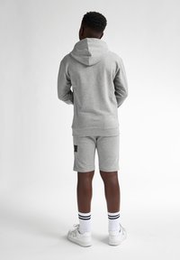 Šedá mikina s kapucí a odpovídající šortky, oba vyrobené z měkké látky. Obsahuje přední klokání kapsu a božní nášivku logo.