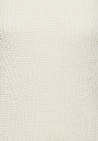 Pull en tricot couleur crème avec une texture côtelée, à coupe décontractée et détails subtils sur les côtés. Le tissu semble doux et chaud.