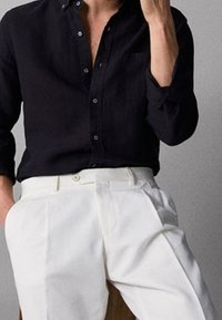 Musta pellavainen napillinen kauluspaita, jossa pitkät hihat ja rintatasku, yhdistettynä valkoisiin laskostettuihin housuihin. Sileä pinta ja räätälöity leikkaus.