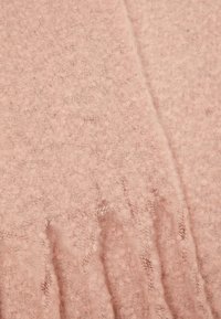 Tissu en laine rose pâle doux avec une texture duveteuse et des coutures visibles le long d'un pli.