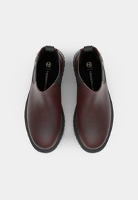 Bruna läderslip-on skor med en slät ytfinish, gummisulor och grå detaljer vid hälen. Timberland-logotyp synlig på innersulan.