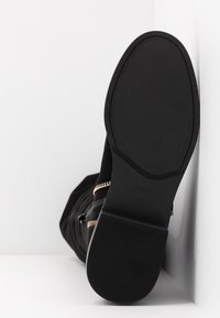 Sort ruskindsankelstøvle med en struktureret sort gummisul, guld lynlåsdetalje på siden og et afrundet tådesign. Størrelse 37.