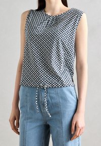 Úzký top bez rukávů v námořnické modré a bílé vzorované látce s uzlem detail při výstřihu, doplněný o světle modré kalhoty s vysokým pasem.