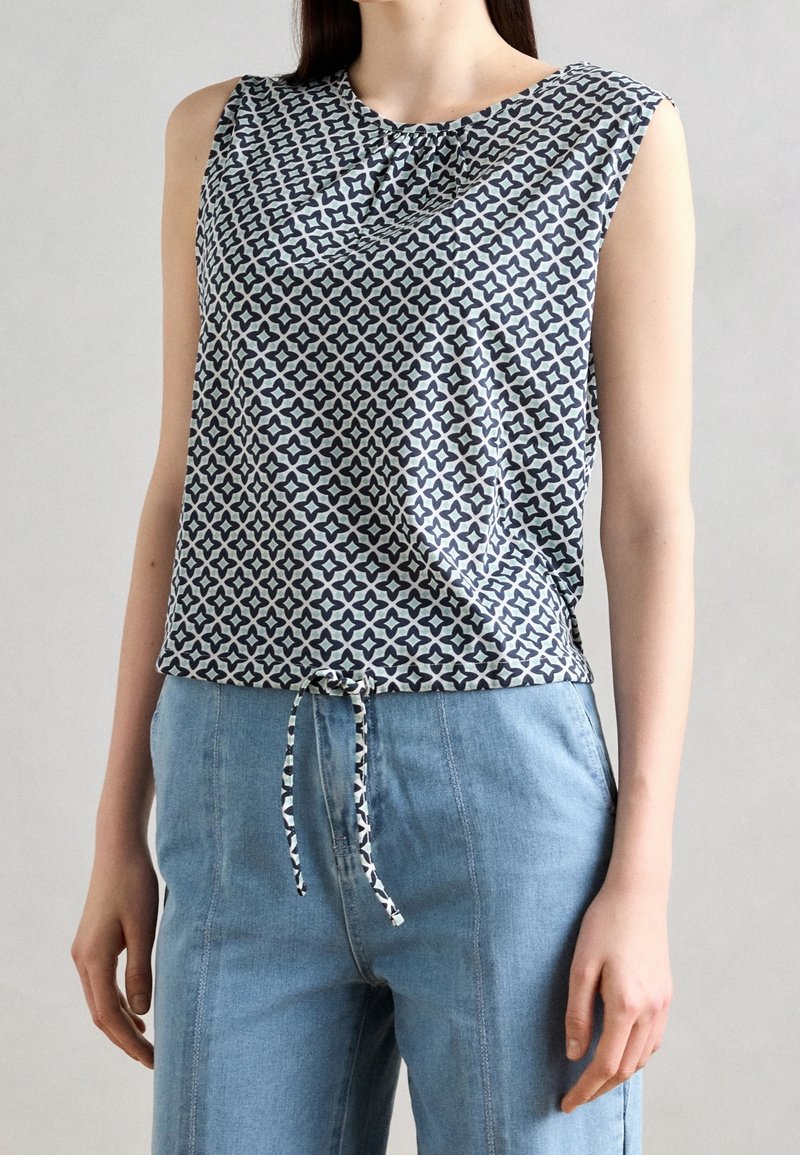 Úzký top bez rukávů v námořnické modré a bílé vzorované látce s uzlem detail při výstřihu, doplněný o světle modré kalhoty s vysokým pasem.