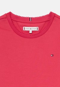 Sarkans kokvilnas T-krekls ar teksturētu virsmu, ar apaļu kakla izgriezumu, dekoratīvu apdari un mazu izšuvu logo uz krūtīm.