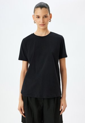 Zwarte katoenen T-shirt met korte mouwen en een ronde halslijn. Bevat reliëftekst op de borst: "Accepteer jezelf." Gladde textuur.