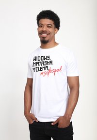 Hvid kortærmet t-shirt med fed sort tekst "WIDOWS. NATASHA. YELENA." og rød tekst "#sistersquad" på forsiden. Glat bomuldsstof.