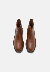 Botine din piele maro, cu panouri elastice pe laterale și o suprafață netedă. Vârf rotunjit și talpă din cauciuc negru contrastant.
