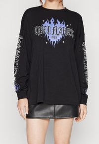 Svart långärmad t-shirt med blå eld grafik, texten "OPEN FLAMES 1992" och vita mönster på ärmarna; kombinerad med en svart läderkjol.