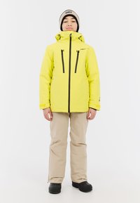 Felgeel waterdicht jack met een capuchon, zwarte ritsen en twee borstzakken. Draag dit met beige broek en zwarte laarzen.