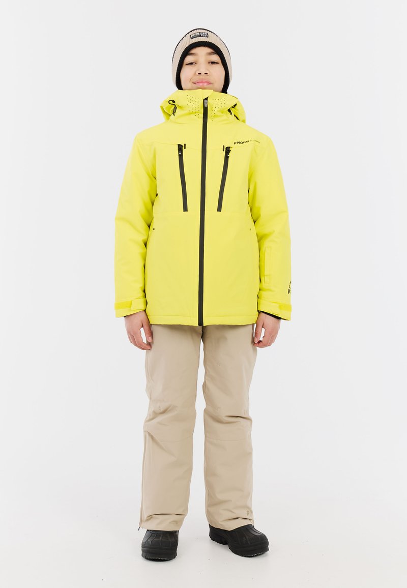 Felgeel waterdicht jack met een capuchon, zwarte ritsen en twee borstzakken. Draag dit met beige broek en zwarte laarzen.