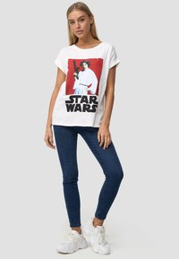 Hvid bomulds t-shirt med rund halsudskæring, der har et grafik af en figur, der holder en blaster, samt tekst der læser "STAR WARS."