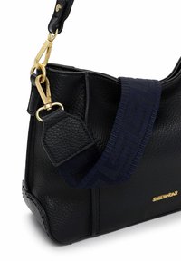 Černá kožená kabelka s hrubou texturou, zlatým kováním a tmavě modrým tkaným páskem s jemným vzorem. Zlaté logo vyražené na boku.