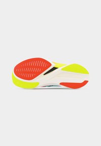 Σόλα λευκού αθλητικού παπουτσιού με κόκκινες και κίτρινες επιφάνειες πρόσφυσης, εμφανιζόμενη από κάτω σε απλό λευκό φόντο.