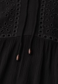 Tissu noir avec broderie florale à œillets, plis texturés et deux cordons suspendus surmontés de perles en bois foncé.