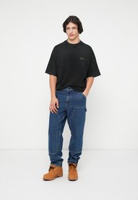 Czarny, oversized t-shirt z krótkim rękawem, w zestawie z niebieskimi dżinsami. Brązowe kozaki z fakturowaną cholewką dopełniają stylizację.