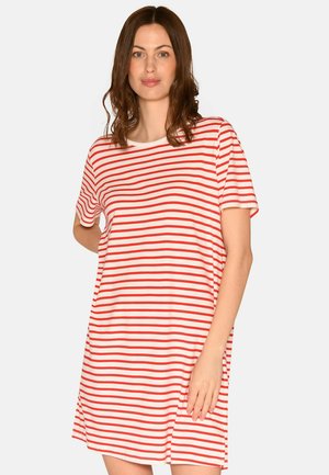 Frau mit braunen Haaren, die ein rot-weiß gestreiftes, kurzärmeliges Kleid trägt und vor einem schlichten hellen Hintergrund steht.