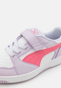 Baskets violettes et blanches avec un logo rose sur le côté, dotées d'une sangle velcro et d'un design à lacets. Fabriquées en cuir avec des accents texturés.