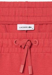 Röda bomullsshorts med elastisk midja och dragsko, Lacoste-logotyp och slät stickad textur. Storlek 36 angiven.