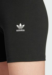 Black ribbed shorts made of stretchy fabric, featuring a small white Adidas logo on the leg. The hem is cleanly stitched.