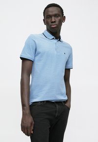 Lichtblauw polo shirt met een zwarte kraag en knoopsluiting. Korte mouwen hebben zwarte accenten. Draagt het met donkere spijkerbroek.