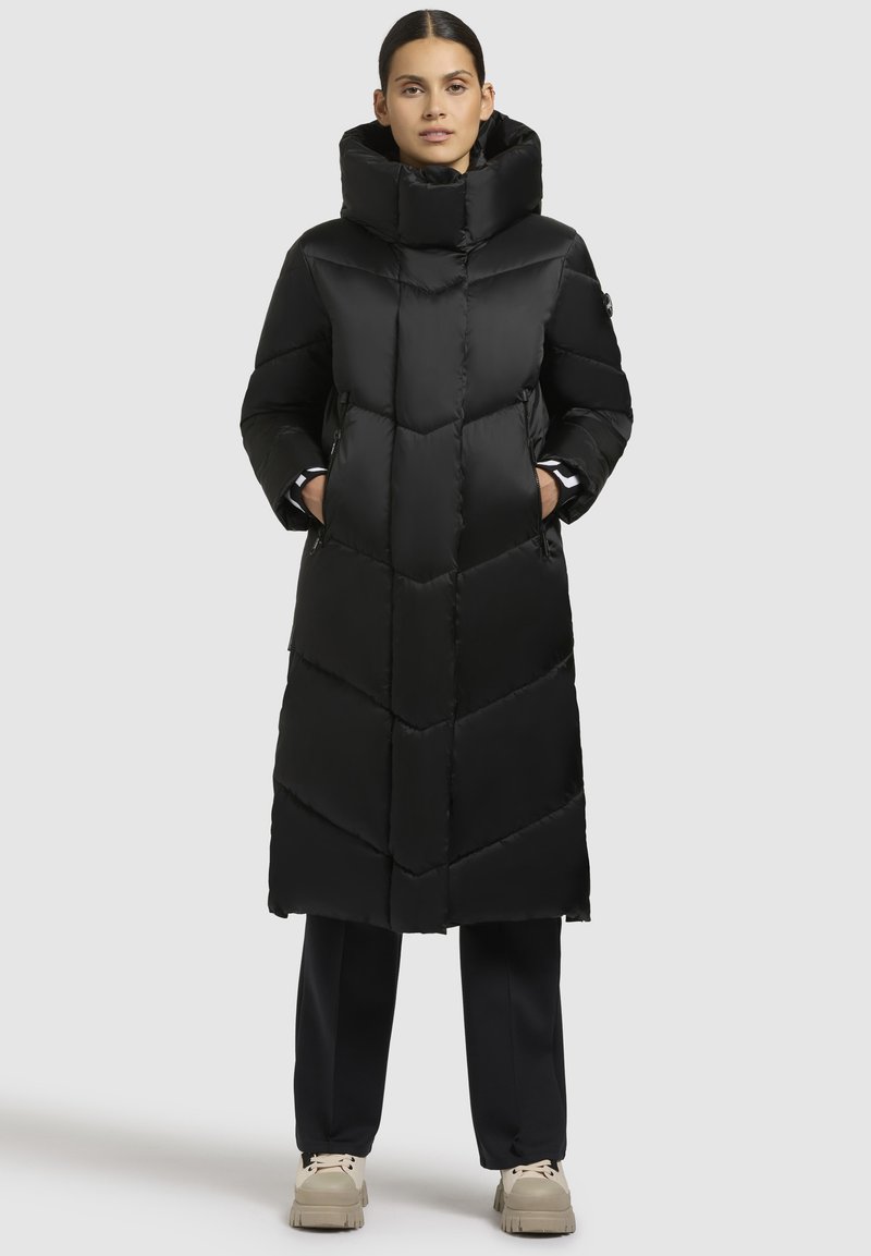 Schwarze Pufferjacke mit hohem Kragen, Zickzackmuster und zwei Seitentaschen. Hergestellt aus glattem, glänzendem Stoff, mit einer langen, schlanken Silhouette.