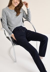 Grijze trui met een ronde hals, gecombineerd met marineblauwe joggingsbroek met trekkoord in de taille en zijzakken, gedragen met witte sneakers.