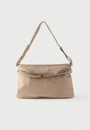Béžová semišová kabelka přes rameno s nastavitelným popruhem, ozdobným páskem se zlatými hroty a kováním na hladkém pozadí.