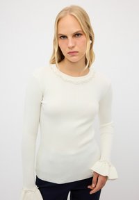 Rippweißes Langarmoberteil mit Rundhalsausschnitt, verziert mit kleinen Perlen entlang des Kragens und glockenförmigen Manschetten.